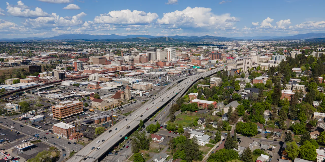 Aerial view of downtown Spokane with Interstate 90 running through the city and wooded hills in the distance.